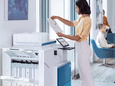A woman checking a printed page at an HP multifunction copier with a finisher