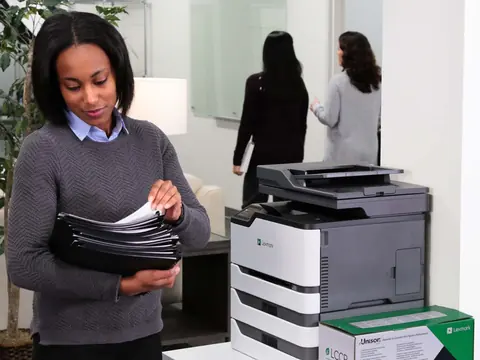A woman sorting folders beside a Lexmark colour multifunction printer