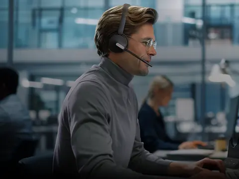 A man at his desk in an open plan office wearing a Yealink wireless headset